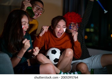 Group Of Asian Friends Sit On Sofa Watching And Cheering Soccer Sports Team On Together TV At Home. Excited Millennial People Sport Fans Celebrate Favorite Football Team Victory In National Match