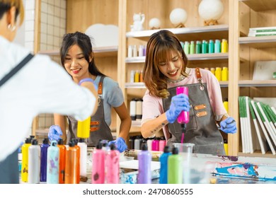 Group of Asian generation z people learning acrylic pouring art on canvas workshop at art studio. Young artist university student enjoy and fun creating colorful abstract modern art painting in class.