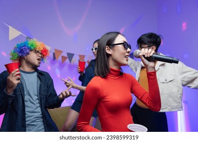 Group of Asian male and female friends They are having fun and dancing together. Sing karaoke at a house party drink cocktails together A room lit up with disco neon lights. New Year's Eve party idea - Powered by Shutterstock