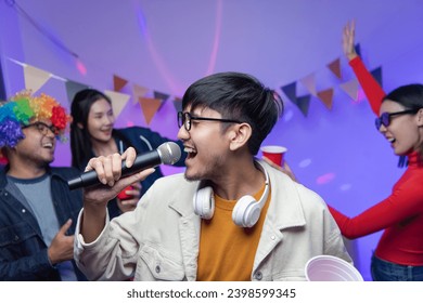 Group of Asian male and female friends They are having fun and dancing together. Sing karaoke at a house party drink cocktails together A room lit up with disco neon lights. New Year's Eve party idea - Powered by Shutterstock