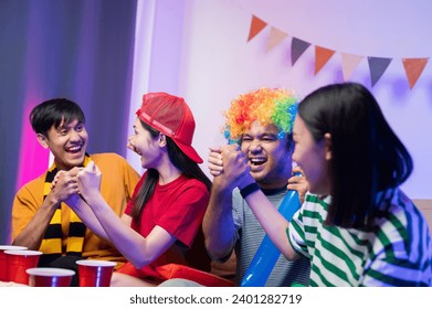 Group of Asian male and female friends Watch the World Cup live broadcast on TV. Sports fans shout and hi five together, celebrating the sports team's victory. and eat snacks together at home - Powered by Shutterstock