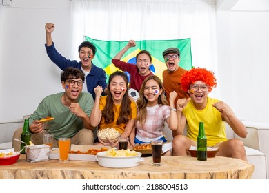 Group Of Asian Man And Woman Friends Watching Soccer Games National Competition On Television With Eating Snack Together At Home. Sport Fans People Shouting And Celebrating Sport Team Victory Match.