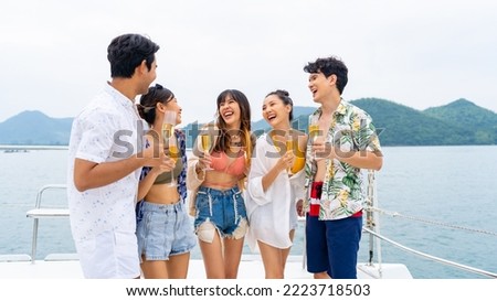 Group of Asian man and woman friends enjoy and fun luxury outdoor lifestyle celebration party drinking champagne together while travel on catamaran boat yacht sailing in the ocean on summer vacation