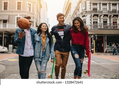 Group of asian men and women walking outdoors with skateboard and basketball. Four friends walking on city street. - Shutterstock ID 1328472641