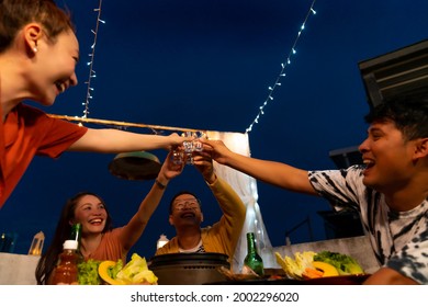 Group Of Asian Millennial People Friends Toasting Alcoholic Drink Shot Glasses While Having Outdoor Dinner Party With Eat Barbecue Grill At Rooftop For Meeting Reunion And Holiday Celebration Together