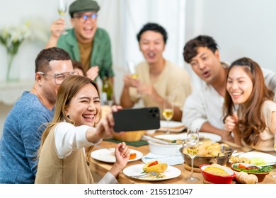 Group Of Asian People Enjoy Dinner Party Eating Food On Dining Table And Using Mobile Phone Taking Selfie Together At Home. Happy Man And Woman Friends Reunion Meeting Celebration On Holiday Vacation