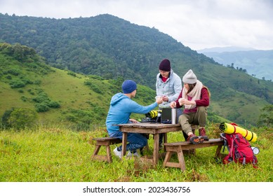 Group Of Asian People Friends With Backpack Enjoy Outdoor Lifestyle Activity In Nature Hiking And Camping Together On The Mountain. Man And Woman Friendship Sit On Outdoor Chair And Drink Hot Coffee 