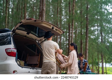 Group of Asian people friends enjoy outdoor lifestyle road trip and camping together on summer holiday travel vacation. Man and woman taking off camping supplies from car trunk at natural park. - Powered by Shutterstock