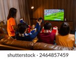 Group of Asian people friends sit on sofa watching and cheering football or soccer games competition on TV together at home.Happy man and woman sport fans celebrating sport team victory sports match