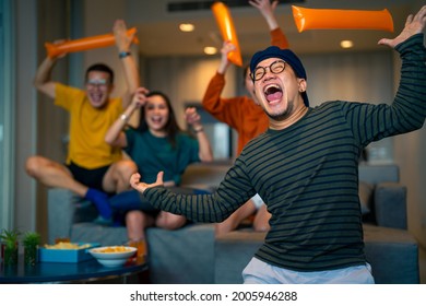 Group Of Asian People Friends Sit On Sofa Watching And Cheering Sports Games Competition On TV Together At Home. Excited Man And Woman Sport Fans Celebrate Sport Team Victory In National Sports Match