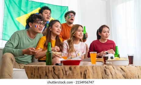 Group Of Asian People Friends Sit On Sofa Watching Soccer Games Competition On TV With Eating Food Together At Home. Man And Woman Sport Fans Shouting And Celebrating Sport Team Victory Sports Match