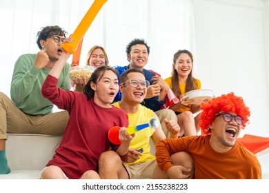 Group Of Asian People Friends Sit On Sofa Watching And Cheering Soccer Games Competition On TV Together At Home. Happy Man And Woman Sport Fans Shouting And Celebrating Sport Team Victory Sports Match