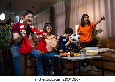 Group Of Asian People Friends Sit On Sofa Watching And Cheering Football Or Soccer Games Competition On TV Together At Home.Happy Man And Woman Sport Fans Celebrating Sport Team Victory Sports Match