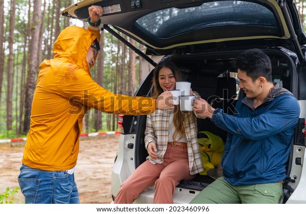 Group of Asian people friends sit on open car\
trunk talking and drinking coffee together at natural park. Man and\
woman friendship enjoy outdoor lifestyle road trip and camping on\
summer vacation.
