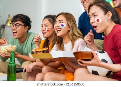 Group Of Asian People Friends Sitting On Sofa Watching Soccer Games Competition On Television With Eating Food Together At Home. Man And Woman Sport Fans Celebrating Sport Team Victory National Match