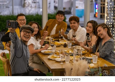 Group of Asian people using mobile phone taking selfie together during outdoor celebration dinner party in the garden on summer holiday vacation. Man and woman friend reunion meeting at restaurant. - Powered by Shutterstock