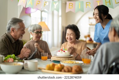 Group Of Asian Senior People Having Birthday Party In A Nursing Home, Celebrating Birthday At Retirement Home With Friends.nurse Giving Birthday Cake To Happy Grandma,who Then Blowing Out Candles