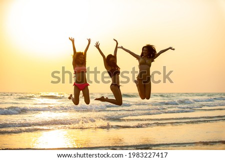 Group of Asian woman friendship in colorful bikini walking and playing on the beach together at summer sunset. Female girl friends enjoy and having fun outdoor activity lifestyle on summer vacation
