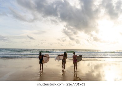 Group Of Asian Woman Surfer In Swimwear Holding Surfboard Walking Together On Tropical Beach At Summer Sunset. Female Friends Enjoy Outdoor Activity Lifestyle Water Sport Surfing On Travel Vacation