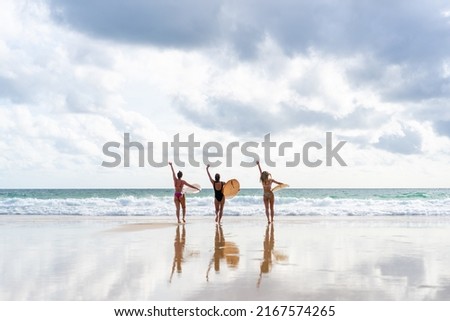 Group of Asian woman surfer in swimwear holding surfboard walking together on tropical beach at summer sunset. Female friends enjoy outdoor activity lifestyle water sport surfing on travel vacation