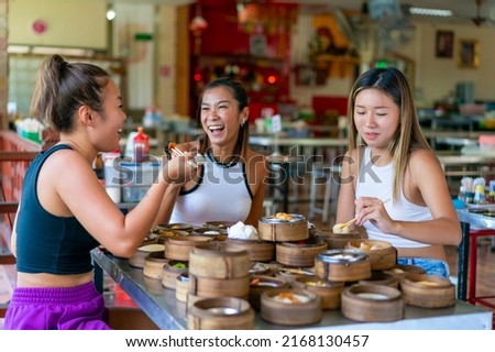 Group of Asian woman tourist eating Chinese food steamed dumpling in bamboo steamer with chopsticks in Chinese restaurant. Happy female friends enjoy eating and travel together on summer vacation.