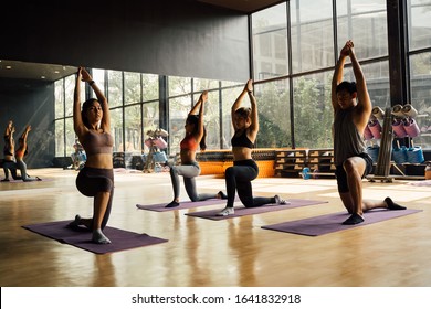 Group Of Asian Women And Man Doing Pilates Lying On Yoga Mats In Aerobics Class. Young Sporty People On Bended Knee On The Floor And Put Hands Up In Gym Studio.