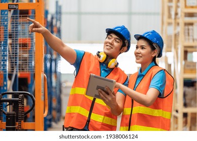 Group Of Asian Young Male And Female Employee Warehouse Worker In Safety Vest And Helmet Working With Tablet For Checking Products Or Parcel Goods On Shelf Pallet In Industry Factory Warehouse