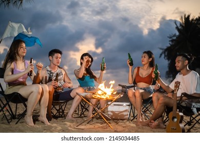 Group Of Asian Young Man And Woman Having Party On The Beach At Night. Attractive Friends Traveler Sing And Dancing While Camping At Seaside Enjoy Holiday Vacation Trip In Tropical Sea Island Together