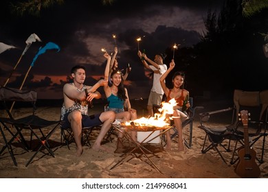 Group Of Asian Young Man And Woman Having Party On The Beach At Night. Attractive Friends Traveler Sing And Dancing While Camping At Seaside Enjoy Holiday Vacation Trip In Tropical Sea Island Together