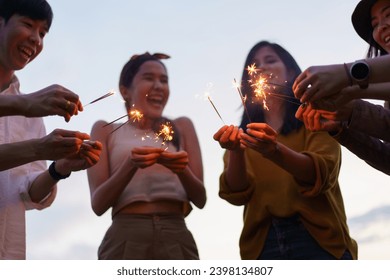 Group of Asian young men and women celebrating together with a sparkling firework in the evening. Happy men and women enjoy playing a sparklers firework in a party. - Powered by Shutterstock