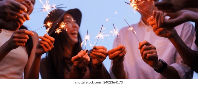 Group of Asian young men and women celebrating together with a sparkling firework in the evening. Happy men and women enjoy playing a sparklers firework in a party. - Powered by Shutterstock