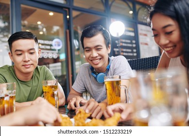 Group Of Asian Young People Sitting At The Table And Laughing While Eating Chicken And Drinking Beer In Cafe