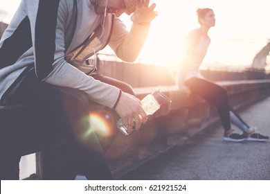 Group Of Athletes Relaxing On The Bench And Resting After Hard Street Workout Session. Man, Woman And Urban Sport. Intentional Lens Flare