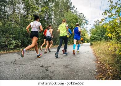 Group Of Athletes Runners Running Marathon In Fall City Park. Yellow Leaves And Blue Sky