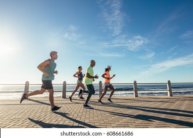 Group of athletes running on ocean front. Runners in sportswear training together outdoors. - Powered by Shutterstock