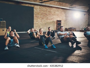 Group of athletic adult men and women performing sit up exercises to strengthen their core abdominal muscles at fitness training - Powered by Shutterstock