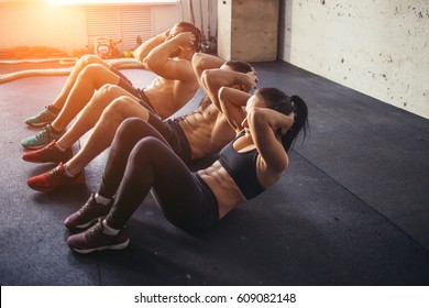 Group of athletic adult men and women performing sit up exercises to strengthen their core abdominal muscles at fitness training