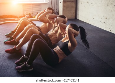 Group Of Athletic Adult Men And Women Performing Sit Up Exercises To Strengthen Their Core Abdominal Muscles At Fitness Training