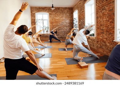 Group of athletic attractive people are practicing yoga class with instructor. Young multiethnic women and men stretch out together in gym. Guys and girls do physical exercises at fitness club. - Powered by Shutterstock