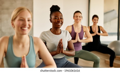 Group Of Athletic Women With Hands Clasped Doing Yoga Exercises In Health Club. Focus Is On Black Woman.