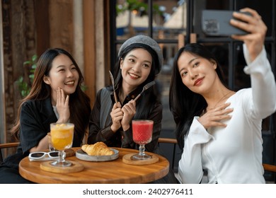 Group of attractive Asian female friends are taking selfies with a smartphone while hanging out at a restaurant or cafe together. City life, travel, lifestyle - Powered by Shutterstock