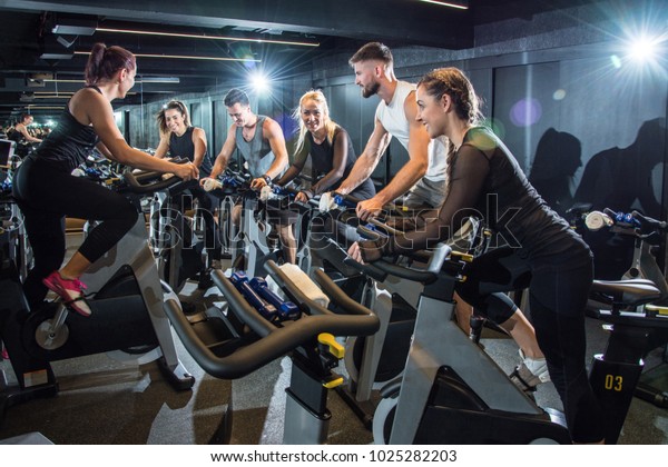 Group of attractive women and men pedaling on a\
stationary bikes at the\
gym.