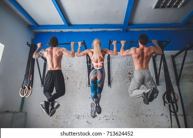 Group of attractive young male and female adults doing pull ups on bar in cross fit training gym with brick walls and black mats - Powered by Shutterstock