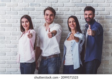 Group Of Attractive Young People, Looking At Camera, Smiling, Showing Thumbs Up On The Background Of A Brick Wall