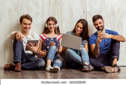 Group of attractive young people sitting on the floor using a laptop, Tablet PC, smart phones, headphones listening to music, smiling - Powered by Shutterstock