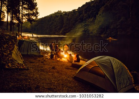 Group of backpackers relaxing near campfire, tourist background.