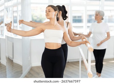 Group of ballerinas preparing performance, learning improving quality of rendering stage. Girls near ballet bare repeat composition including third position with guidance mature female mentor