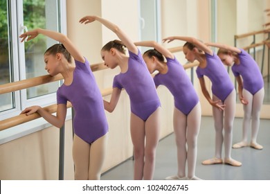 Group of ballerinas training at ballet barre. Young ballet girs in purple leotards practicing at ballet class. Tips for beginning ballet.