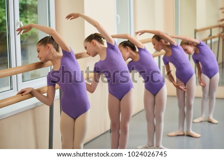 Group of ballerinas training at ballet barre. Young ballet girs in purple leotards practicing at ballet class. Tips for beginning ballet.