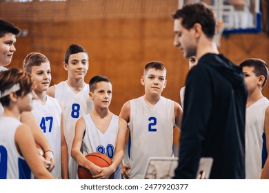 A group of basketball players focus intently during a team discussion with their coach in a gym, illustrating a moment of sport strategy - Powered by Shutterstock